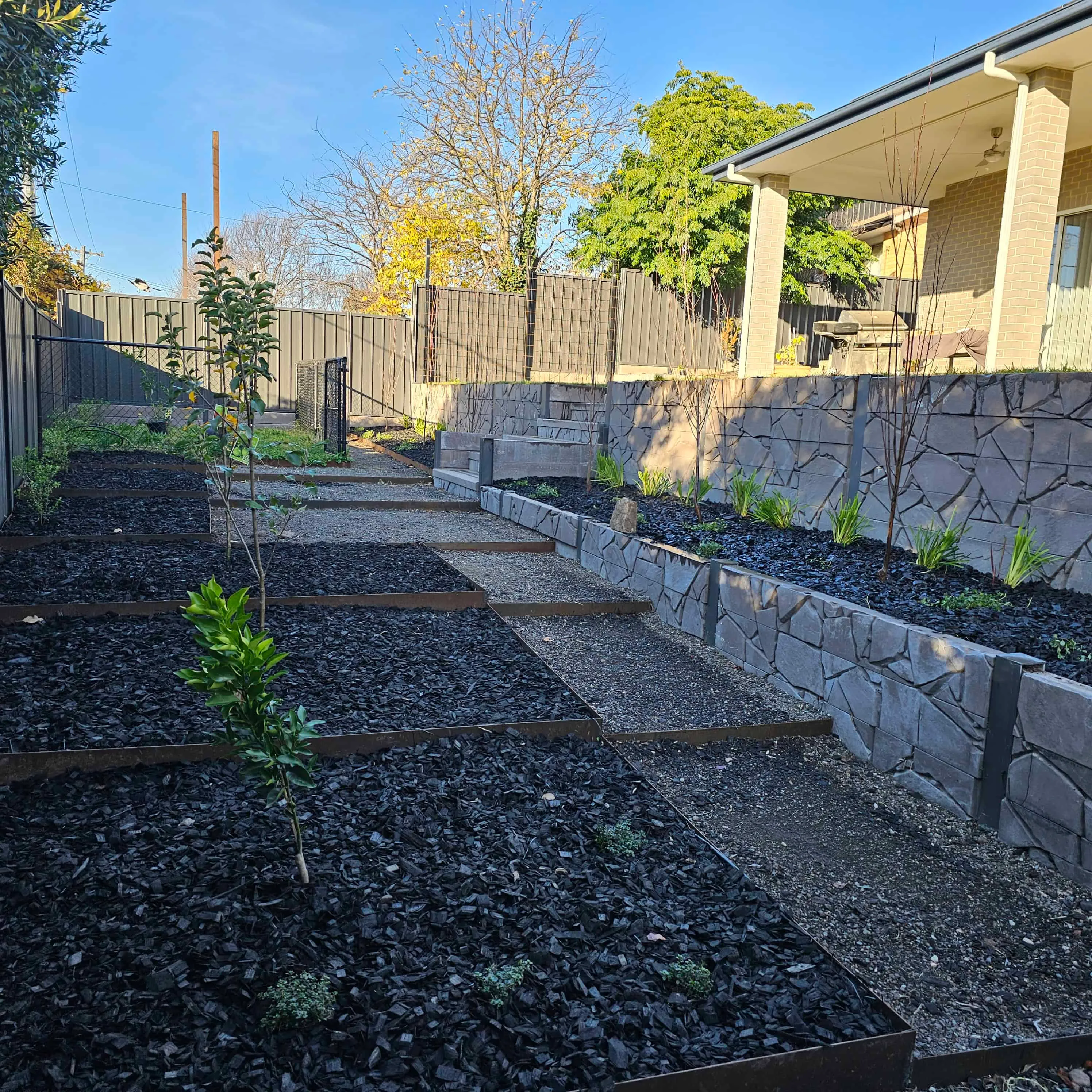 A finished Canberra landscape with a stone retaining wall, sculpted garden beds and fresh lawn by Dust To Lawn