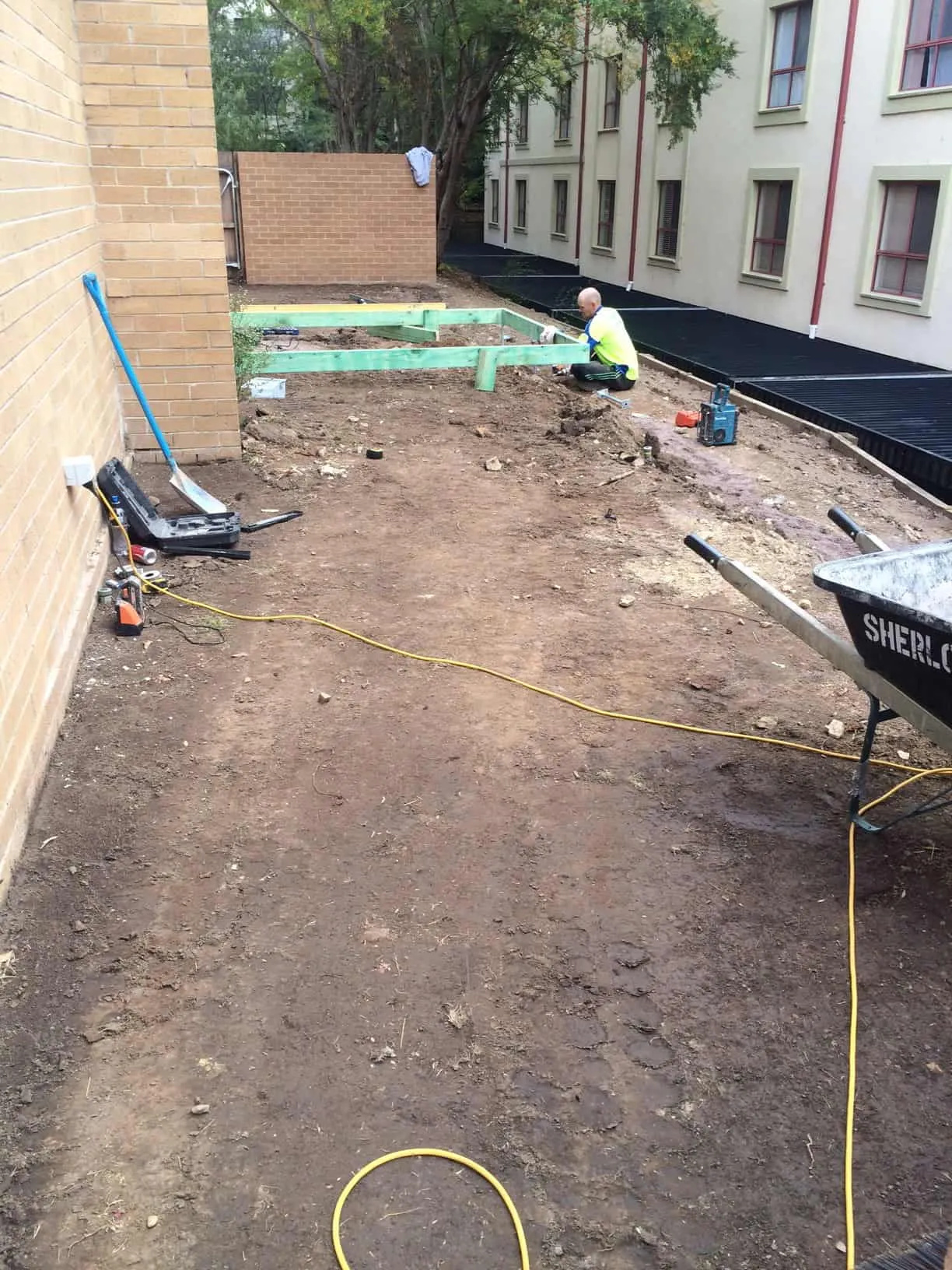 A raw dirt strip beside a brick unit block before Dust To Lawn
